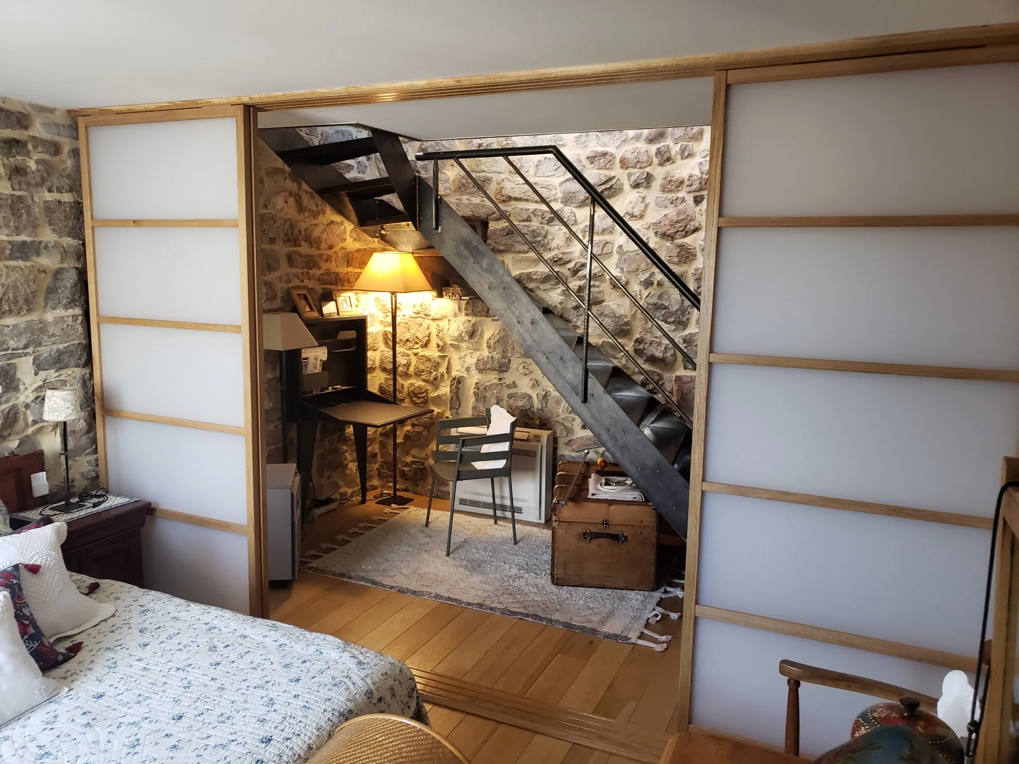 Cloison avec portes coulissantes en bois et panneaux blancs, séparant une chambre et un espace bureau, idéal pour un aménagement intérieur harmonieux. ​​